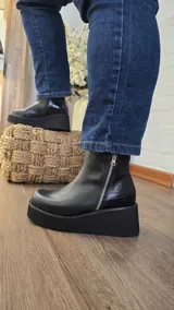 Botas de cuero negro con plataforma alta, cierre lateral plateado y panel trasero con textura símil reptil.