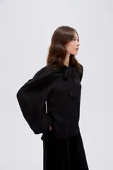 Camisa de poliéster color marfil, de diseño holgado, con cuello alto lazada y mangas largas abullonadas.