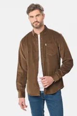 Camisa de pana fina en color verde oscuro, de manga larga con puños arremangados, cuello camisero con botones y un bolsillo aplicado en el pecho con pequeña etiqueta decorativa.