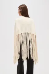 Poncho de punto color crudo con cuello alto y diseño de flecos largos en el ruedo.