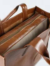 Cartera de cuero color marrón con compartimiento interno removible y logo circular en el frente.