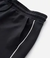 Pantalón deportivo de corte recto y estilo holgado, color negro con una línea vertical blanca en los laterales. Cuenta con cintura elástica con cordón de ajuste y bolsillos laterales.