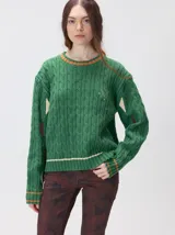 Sweater de punto con diseño de ochos en color verde, cuello redondo con detalle de franja en contraste, y apliques de rombos en las mangas. Presenta un bordado con la letra M en el pecho.