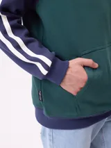 Canguro con capucha de estilo deportivo, con cuerpo en color celeste y mangas raglán en color negro. Presenta el logo de la marca estampado en el pecho, bolsillo tipo canguro frontal y franjas blancas laterales en las mangas.