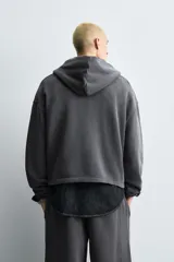 Sudadera con capucha y cierre frontal de cremallera, confeccionada en tejido con efecto lavado. Presenta un corte relajado, bolsillos tipo canguro y parches decorativos en el pecho. Las mangas largas terminan en puños de rib.