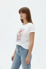 Remera blanca de manga corta y cuello redondo, con diseño estampado en el frente que simula un sello postal con palmeras y la inscripción 'la paloma'.