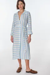 Vestido camisero midi a rayas verticales celestes y blancas, con cuello camisero, mangas largas con puños acampanados y cinturón de lazo.