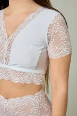 Conjunto de lencería blanco compuesto por un corpiño corto con mangas cortas y detalles de encaje floral en el escote y bajo busto, y una bombacha hipster tiro alto completamente de encaje.