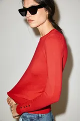 Sweater de punto liso color rojo, con cuello redondo, manga larga y detalles de botones dorados en los puños.