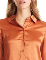 Camisa de satén color verde oliva, con cuello clásico, cierre frontal con botones metálicos y mangas largas con puños abotonados.