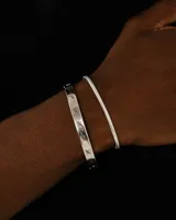 Pulsera rígida plateada con cierre de bisagra y grabados de líneas verticales.