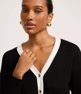 Cardigan de punto blanco con escote en V, botones metalizados, bolsillos falsos, cuello y vista contrastantes en negro, y bajo acanalado.