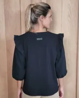 Remera blanca de algodón con cuello redondo, mangas tres cuartos abullonadas y detalle de volados en los hombros.