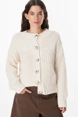 Saco de punto grueso color chocolate, con cuello redondo, cierre frontal con botones grandes y diseño de textura acanalada. Presenta un calce relajado y mangas largas con puños ajustados.