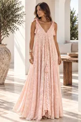 Vestido largo color dorado, confeccionado en tela semitransparente con diseño bordado floral y detalles de brillo. Presenta escote en V, tirantes finos ajustables con borlas en los hombros, y corte amplio y fluido con gran movimiento.