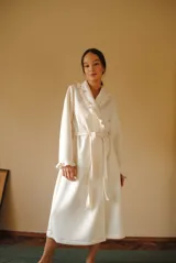 Bata larga color blanco, confeccionada en algodón capitoneado con diseño de espiga. Presenta volados en el cuello y puños, y lazo de ajuste en la cintura.