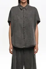 Camisa de corte capa confeccionada en mezcla de lyocell y algodón, en color gris con efecto acid wash. Presenta cuello camisero, cierre frontal con botones y mangas cortas de caída amplia.