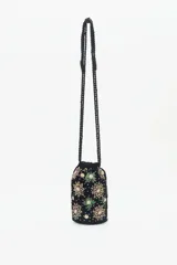 Cartera tipo bolso de mano color negro, confeccionada en terciopelo con bordados de estrellas y aplicaciones de pedrería brillante. Cuenta con correas trenzadas de cordón negro y cierre superior.