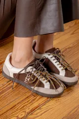 Championes de estilo urbano en combinación de tonos marrones y crema, confeccionados en gamuza y cuero. Presentan cordones jaspeados, suela de goma y detalle de logo bordado en el lateral.