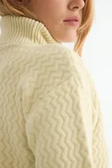 Polera de tejido de punto con cuello alto y textura acanalada en zigzag. Presenta mangas largas y puños ajustados, con un diseño clásico y versátil.