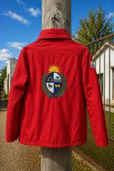 Campera impermeable de tela taslon color negro, con diseño de cuello alto y cierre frontal. Presenta un gran bordado en la espalda que incluye el escudo nacional uruguayo y el logo de la marca Bagual, además de un parche circular con la bandera de Uruguay en la manga.