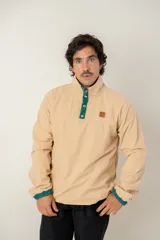 Buzo de pana color beige, de corte oversize, con cuello alto y cierre frontal parcial con botones a presión. Presenta detalles en color verde en la tapeta de los botones y en los puños, además de un parche decorativo en el pecho.