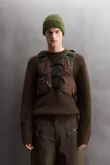 Chaleco deportivo técnico de malla transpirable en color negro, diseñado para running y actividades al aire libre. Cuenta con múltiples compartimentos, bolsillos con cremalleras termoselladas, cierres frontales de hebilla de liberación rápida y ajuste lumbar mediante cordón elástico.