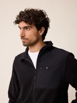 Campera de polar color beige con cierre frontal completo y cuello alto. Presenta un bolsillo en el pecho con cierre y detalle de parche con logo. El diseño combina paneles de tejido polar con detalles en tejido técnico en la zona del pecho.