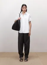 Camisa blanca de algodón con diseño recto, cuello camisero, manga corta y cierre frontal de botones ocultos con tapeta.