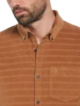Camisa marrón de corderoy con diseño de líneas horizontales, corte slim fit, cuello abotonado, manga larga, bolsillo plaqué en el pecho y cierre frontal con botones.