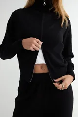Conjunto de dos piezas tejido en color crema, compuesto por un cárdigan con cierre frontal completo y cuello alto, y pantalón de corte recto con cintura elástica.