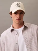Gorra de béisbol color crema o blanco roto, confeccionada en algodón, con visera curva y bordado frontal grande del monograma 'CK' en color negro.