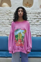 Buzo oversized color rosa con sisas caídas y mangas con detalle de tablas que aportan volumen. Presenta una estampa central estilo vintage con motivos de verano.