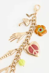 Llavero decorativo para bolso con cadena de eslabones dorados y múltiples dijes colgantes, incluyendo una mano, un corazón con símbolo de paz, un pez y cuentas de vidrio de colores.