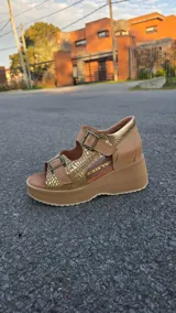 Sandalias de cuero color tostado con plataforma y taco chino, tiras frontales y laterales con hebillas ajustables y detalles en tono dorado texturizado.
