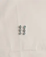 Aros colgantes de plata 950 con tres piedras naturales facetadas de topacio en tono celeste, dispuestas en secuencia vertical con engarces de contorno irregular.