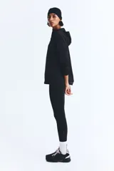 Campera deportiva de running color negro, confeccionada en tejido funcional DryMove. Presenta un diseño de corte holgado con medio cierre frontal, capucha de doble capa, mangas raglán con abertura para el pulgar y bolsillos laterales con cierre. Incluye cordón elástico ajustable en el bajo y detalles reflectantes.