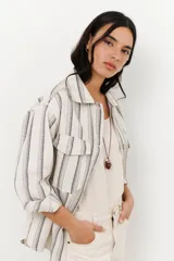 Chaqueta de algodón a rayas verticales en tonos beige y gris, con cuello camisero, cierre frontal con botones y mangas largas con puños abotonados. Tiene bolsillos delanteros con solapa y galones ondeados a tono.