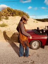 Bolso marrón de gamuza con flecos largos, asa de hombro y detalle de pasamanería con nudos.