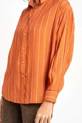 Camisa oversize color ladrillo con rayas verticales blancas y rosadas, de mangas largas y botones de madera.