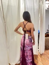 Vestido largo sin mangas con escote en V halter y aberturas laterales (cut-outs) en la cintura. El cuerpo superior presenta un llamativo diseño estampado multicolor, mientras que la falda larga es de tejido texturizado brillante en color verde esmeralda con inserciones godet en el ruedo.