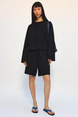 Bermuda de algodón color negro, con tiro medio, cintura elástica ajustable con cordones y bolsillos laterales ocultos en costura.