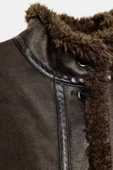 Chaqueta bomber de cuello alto con forro interior de pelo sintético. Presenta cierre frontal con botones, bolsillos delanteros y bajo ajustable con cordones.
