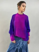 Buzo tejido de lana merino con diseño oversize, manga ranglan y cuello levemente elevado. Presenta un degradado de color vibrante en tonos violeta y fucsia.