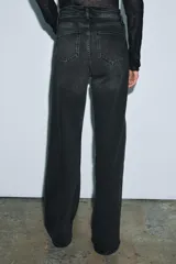 Jeans de tiro alto con corte wide leg y largo completo. Presenta diseño de cinco bolsillos, trabillas en la cintura y cierre frontal con cremallera y botón, con un acabado de efecto lavado.