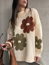 Sweater de tejido de punto color natural, con diseño de flores grandes aplicadas en tonos marrón y verde oliva. Presenta cuello redondo, mangas largas y corte holgado.