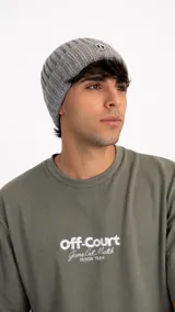 Gorro tipo beanie de punto acanalado en color gris, con parche circular bordado en la parte frontal.