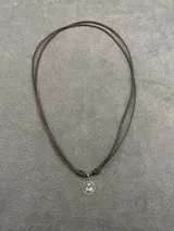 Collar con medalla circular plateada que representa el Sagrado Corazón, montada sobre un cordón encerado de color marrón con nudos ajustables.