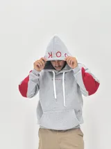 Canguro gris con capucha, de corte holgado, con detalles en color rojo en las mangas y estampado de texto en color rojo en la capucha y el pecho.