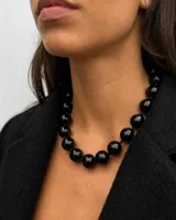 Collar de esferas negras de resina con acabado brillante, ensartadas en hilo negro. Presenta un cierre tipo marinero en color dorado.